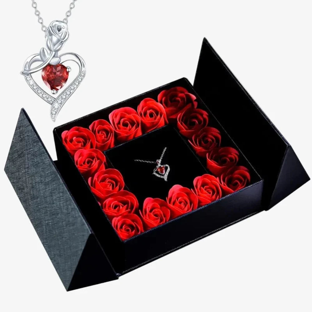 Boîte noire ouverte entourée de roses rouges disposées en carré, pendentif cœur argenté avec pierre rouge au centre