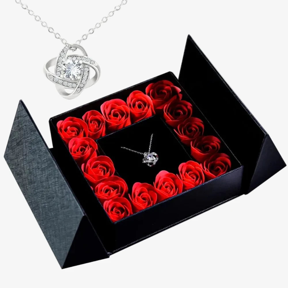 Pendentif nœud infini argenté avec pierre transparente, boîte noire ouverte entourée de roses rouges disposées en carré
