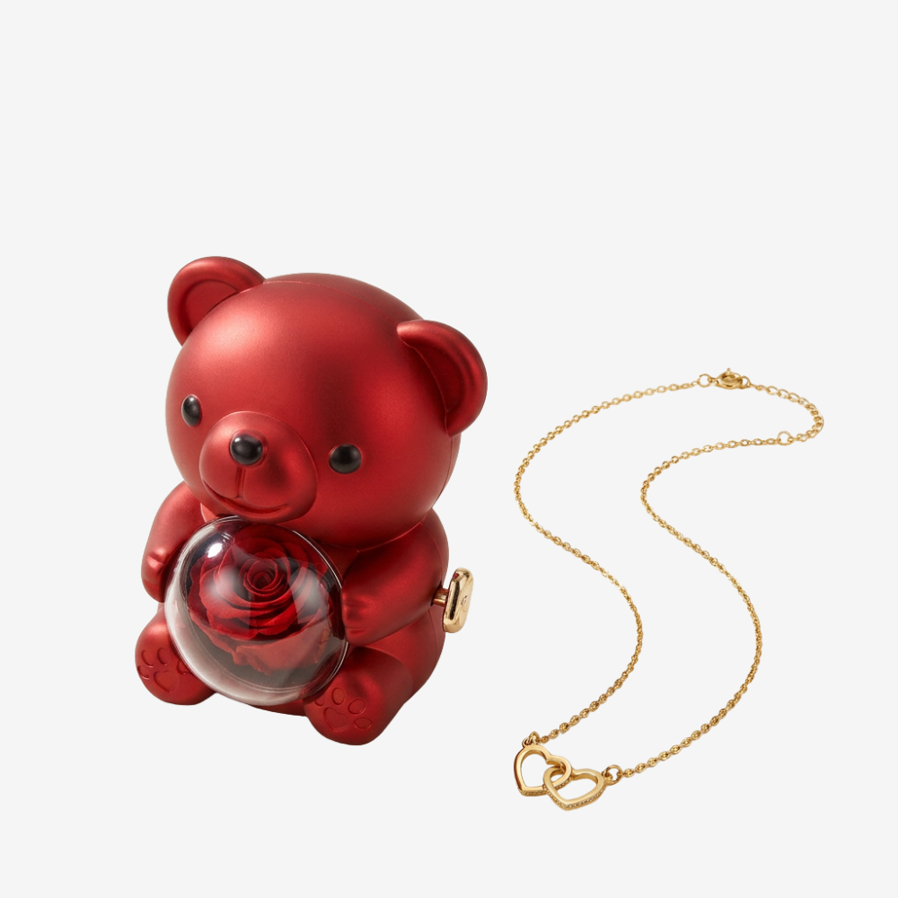 Boîte ourson rouge métallisé tenant une sphère en verre avec rose, collier cœurs entrelacés dorés posé à côté