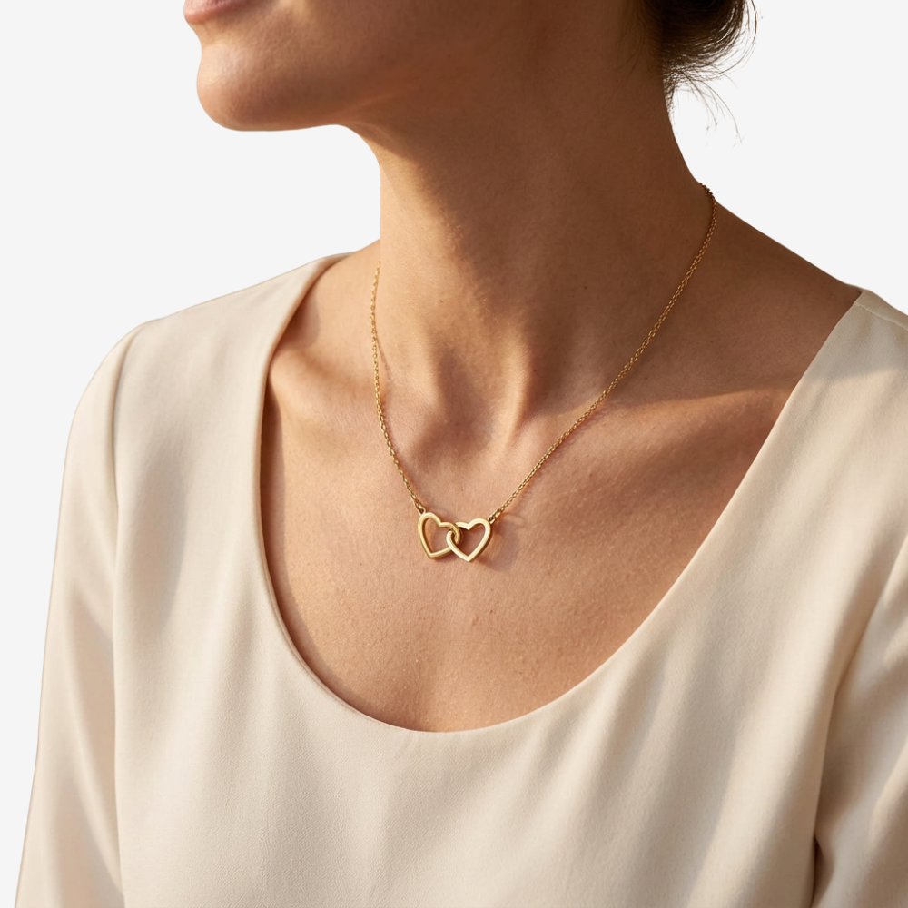 Collier porté sur décolleté, pendentif cœurs entrelacés dorés sur modèle en haut crème