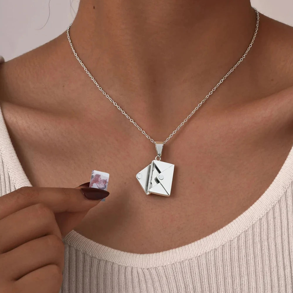 Collier avec photo porté au cou, main insérant une photo dans l'enveloppe argentée