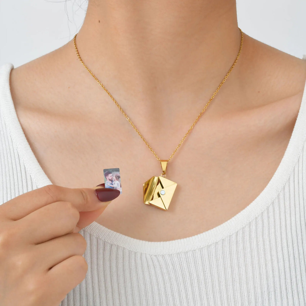 Collier avec photo porté au cou, main insérant une photo dans l'enveloppe dorée