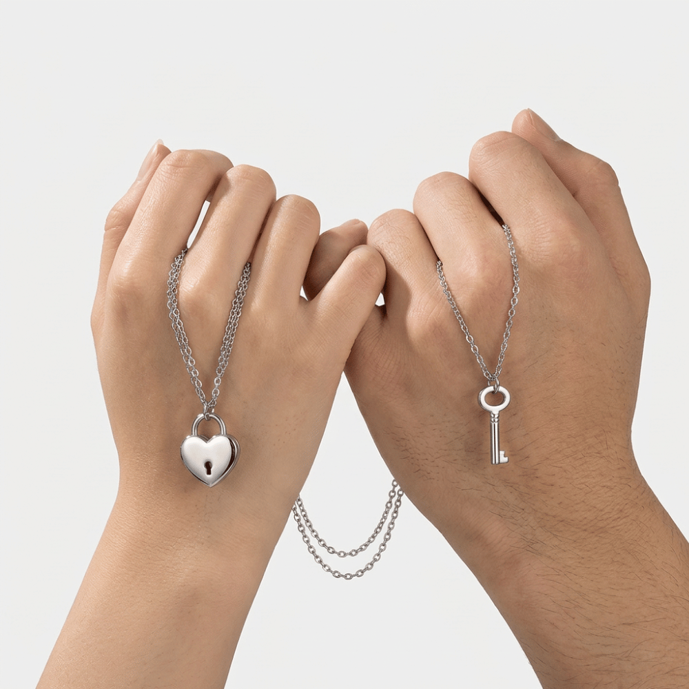 Collier de couple tenu par deux mains, pendentifs cadenas cœur et clé argentés