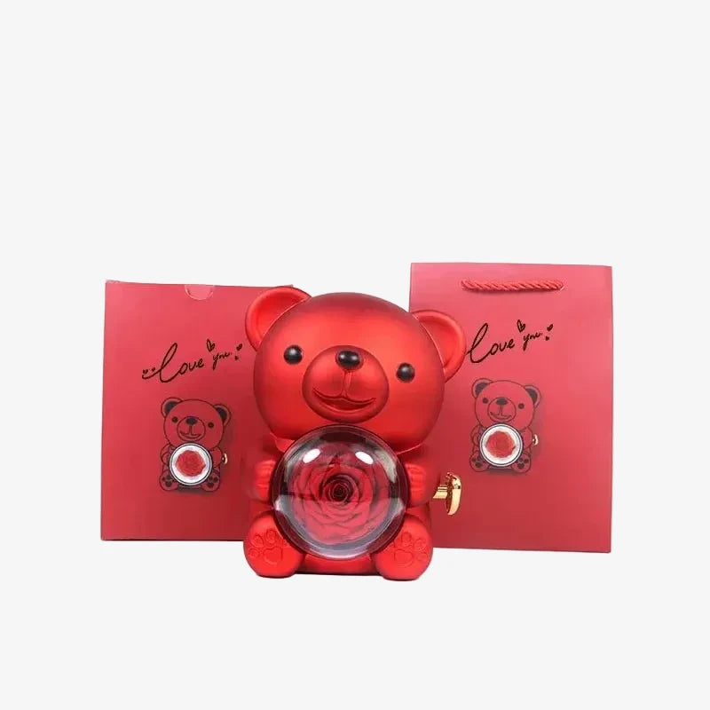 Ourson rouge avec sphère à rose encadré par deux sacs cadeaux rouges assortis Love you