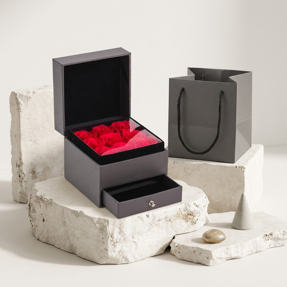 Boîte cadeau bijou avec roses éternelles posée sur décor minéral ivoire