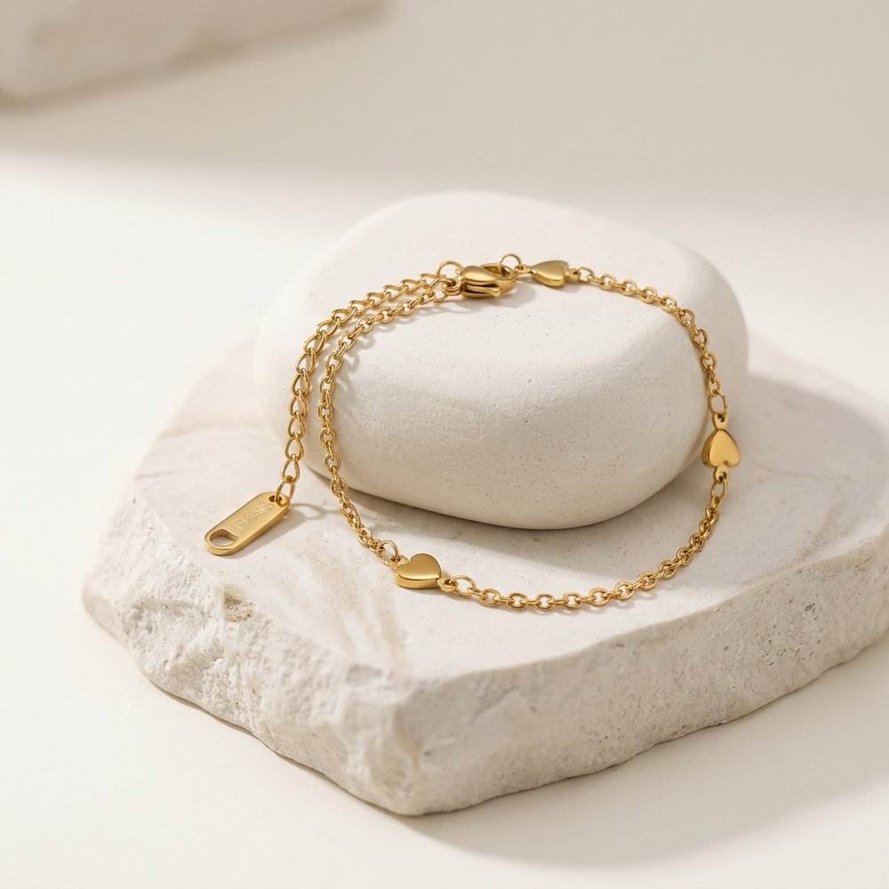 Bracelet cœur doré, posé sur un support minéral ivoire