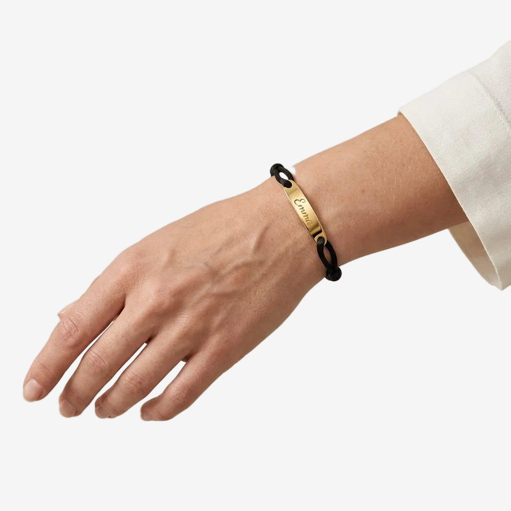 Bracelet corde personnalisable porté au poignet, cordon noir et plaque dorée gravée