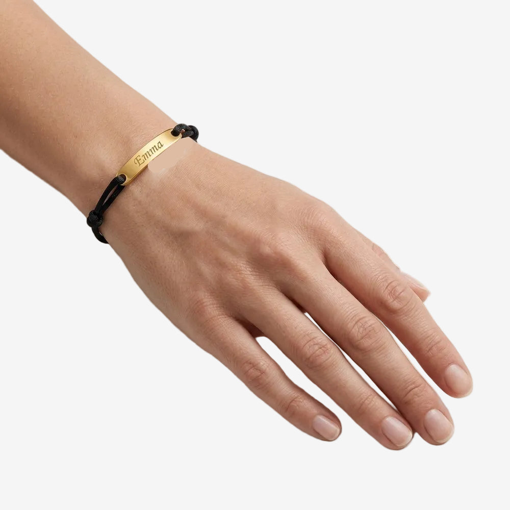 Bracelet cordon femme à plaque gravée, geste de main au poignet sur fond neutre