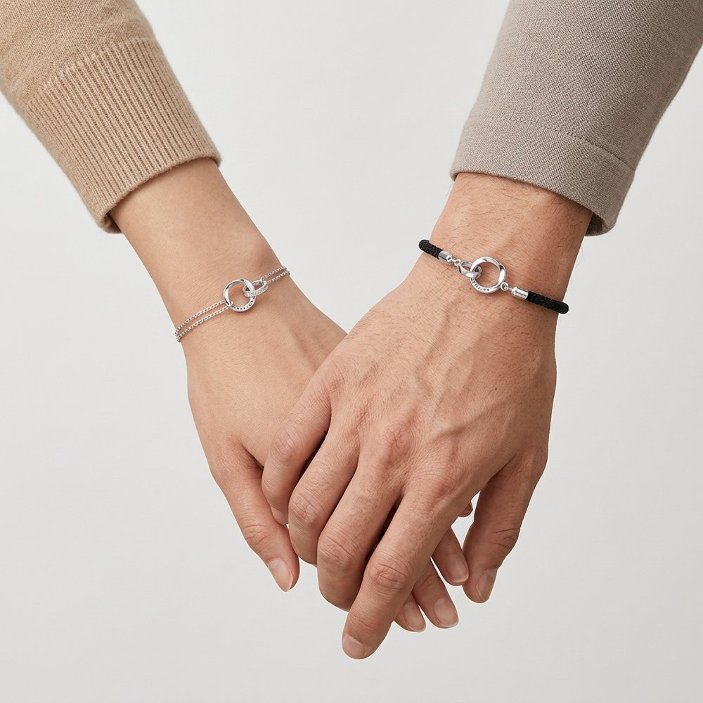 Bracelet duo couple porté par deux mains liées, chaîne argentée et cordon noir à anneaux entrelacés