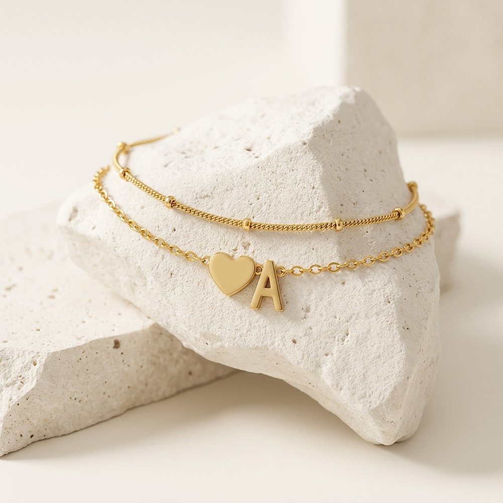 Bracelet femme cœur avec une lettre, posé sur un support minéral ivoire
