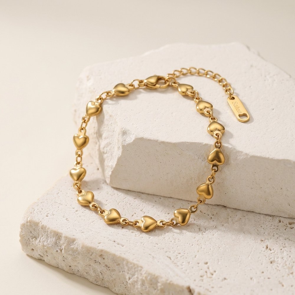 Bracelet femme cœur doré, posé sur un support minéral ivoire