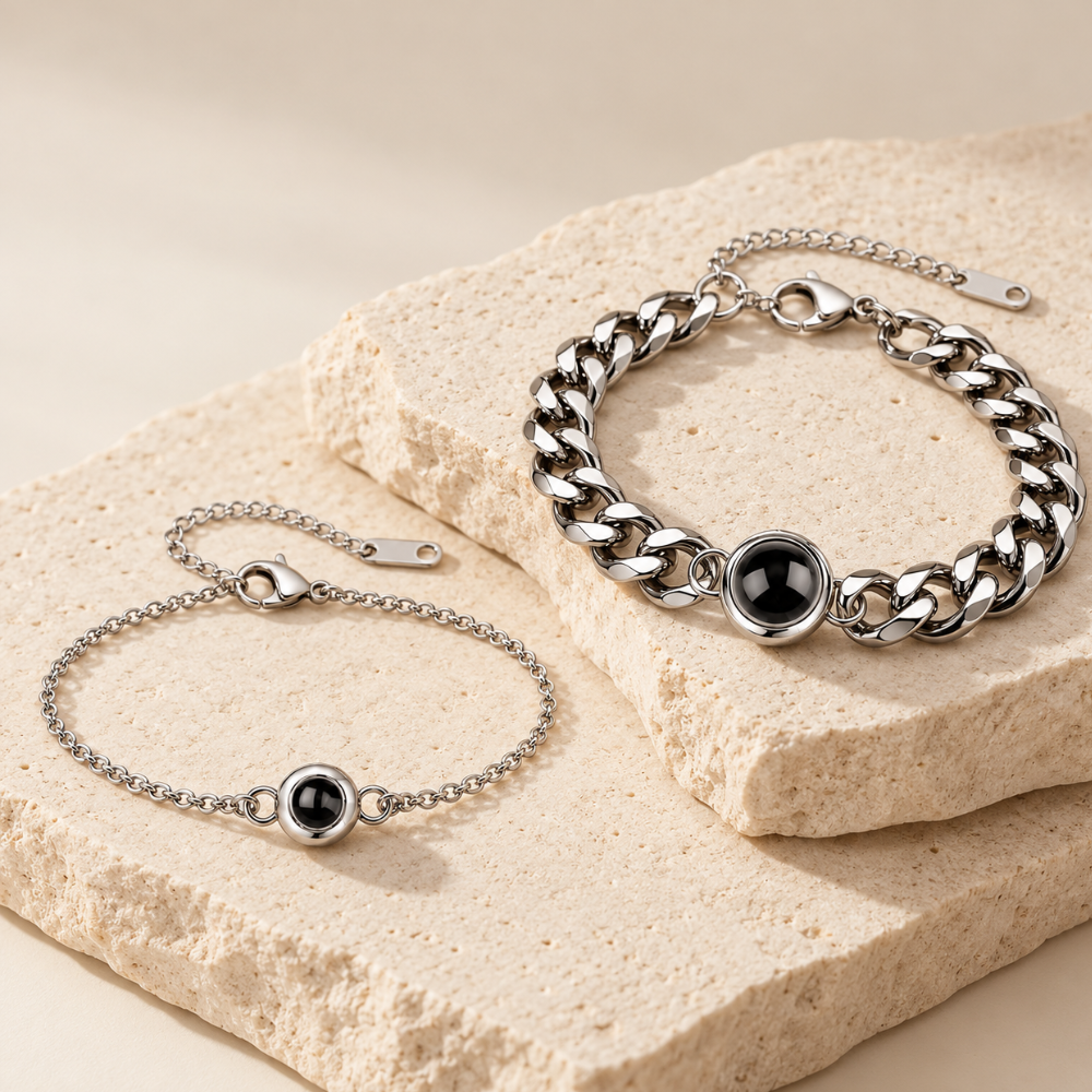 Deux bracelets photo projection, chaîne femme et gourmette homme en acier inoxydable, posés sur un support minéral beige