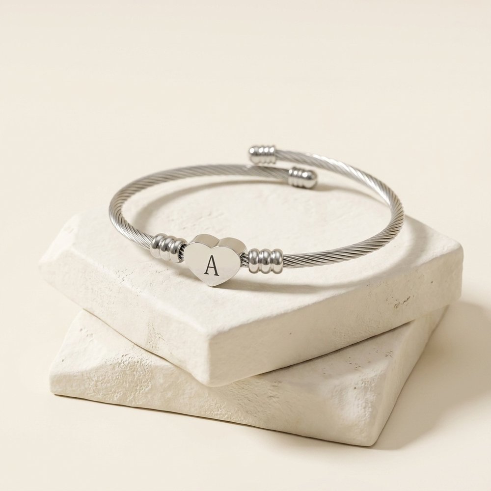 Bracelet manchette cœur initial, posé sur un support minéral ivoire
