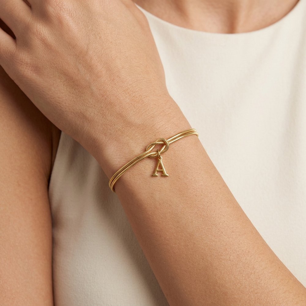 Bracelet noeud initial doré porté au poignet, lettre A suspendue au nœud d'amour