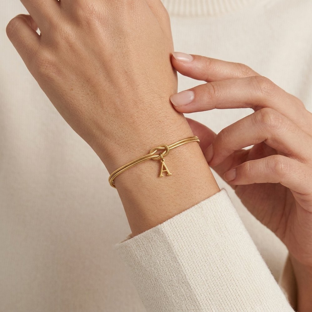 Bracelet initiale femme en chaîne serpent dorée, geste de main sur fond neutre