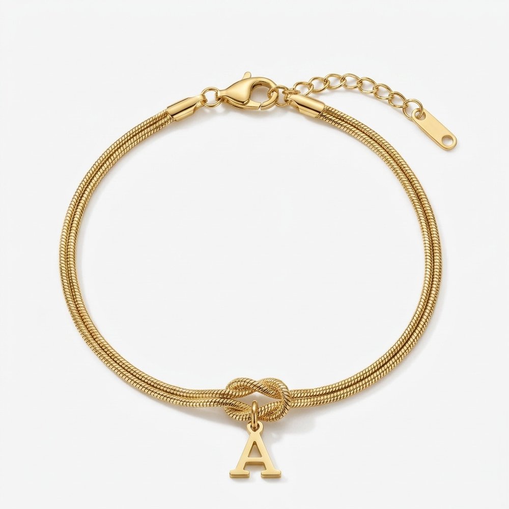 Bracelet lettre en chaîne serpent dorée avec nœud d'amour et initiale A, vue produit sur fond neutre