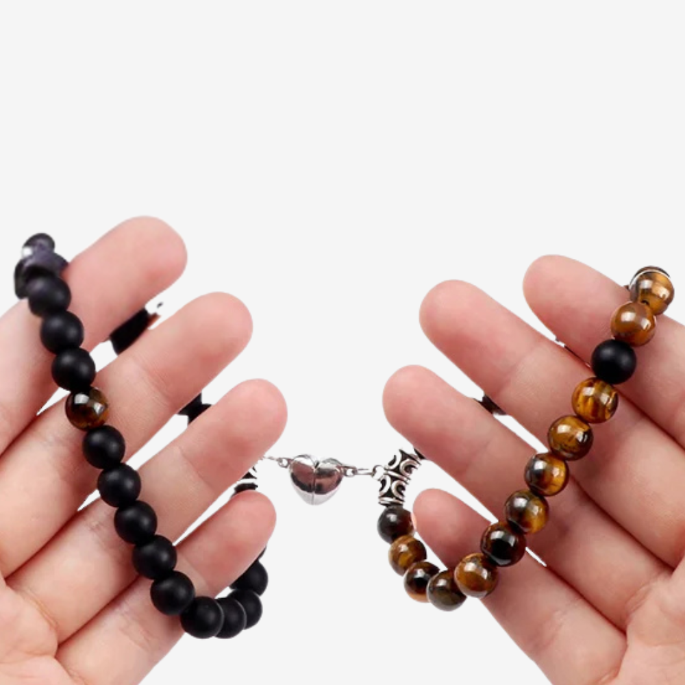 Bracelet d'amour porté par deux mains, aimant cœur reliant perles noires et œil-de-tigre