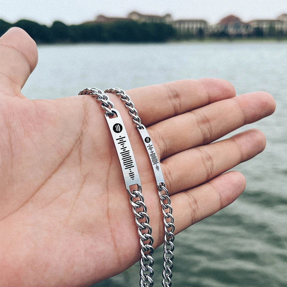 Bracelet couple en commun tenu dans la main, plaques gravées de codes Spotify
