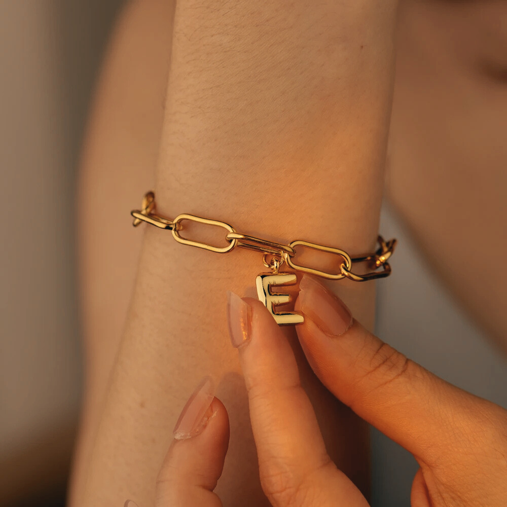 Bracelet lettre femme porté au poignet, gros plan sur le charm initiale doré