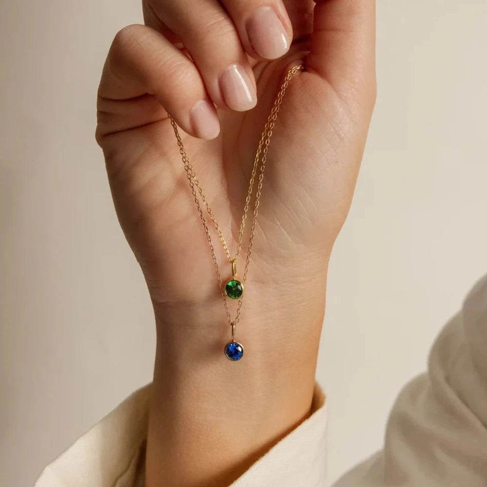 Une main de femme qui entre ses doigts porte deux colliers pierre de naissance