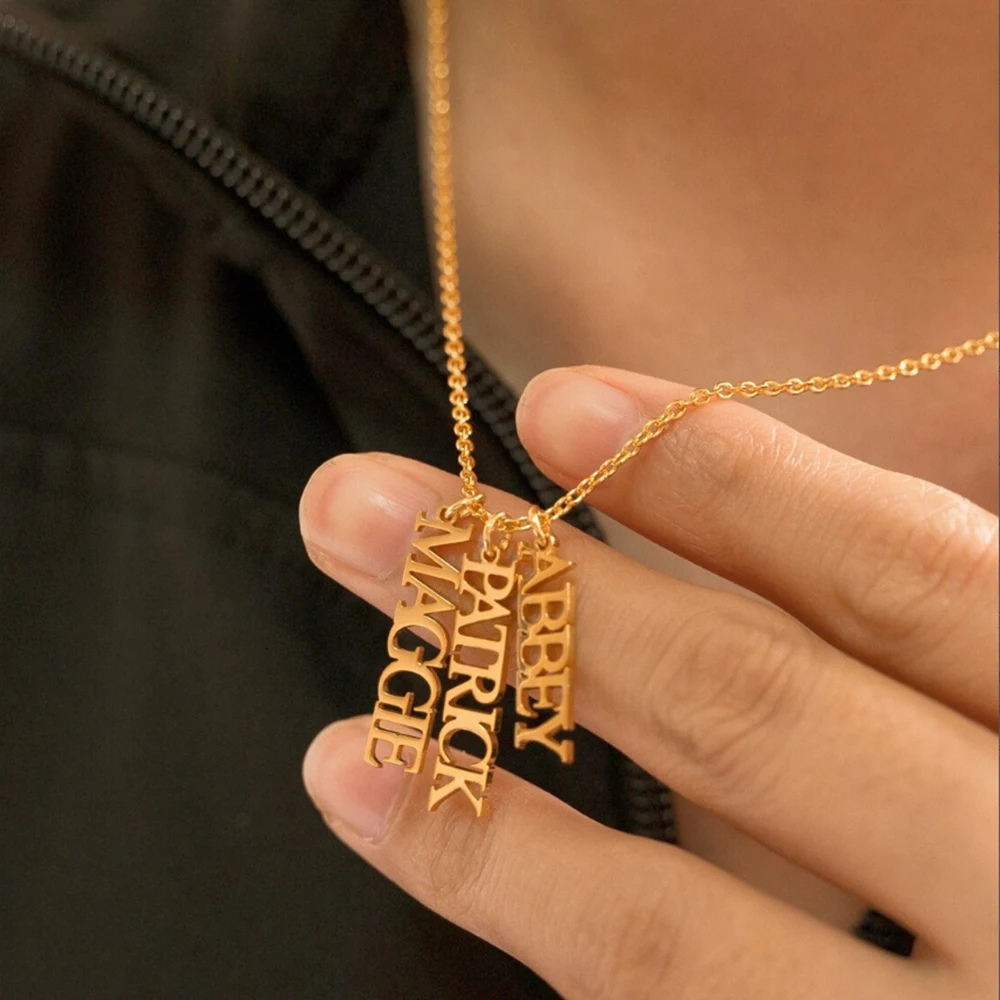 Collier prénoms personnalisés tenu dans la main, gros plan sur les pendentifs dorés