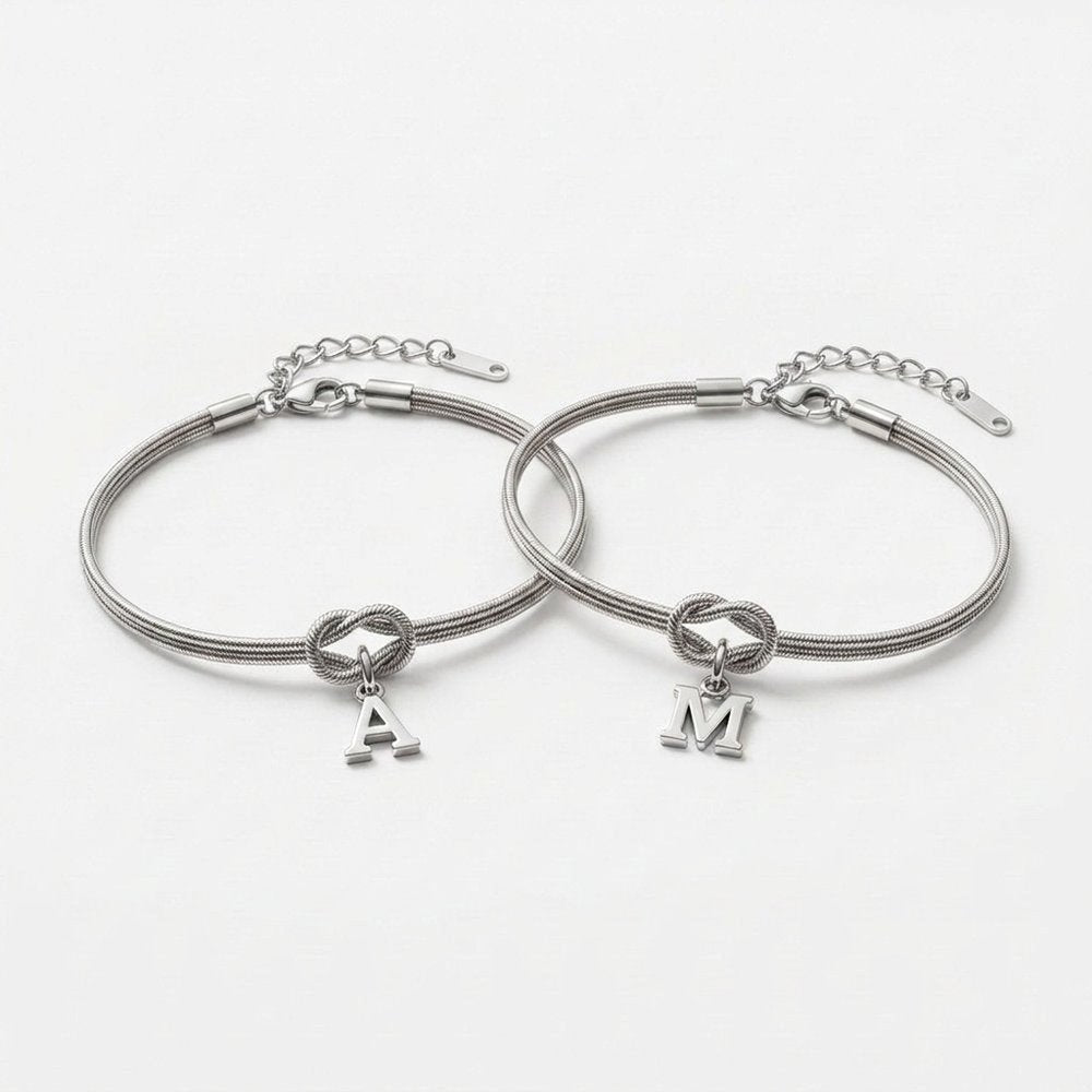 Duo de bracelet noeud : deux chaînes serpent argentées avec nœud d'amour et initiales A et M, vue produit sur fond neutre