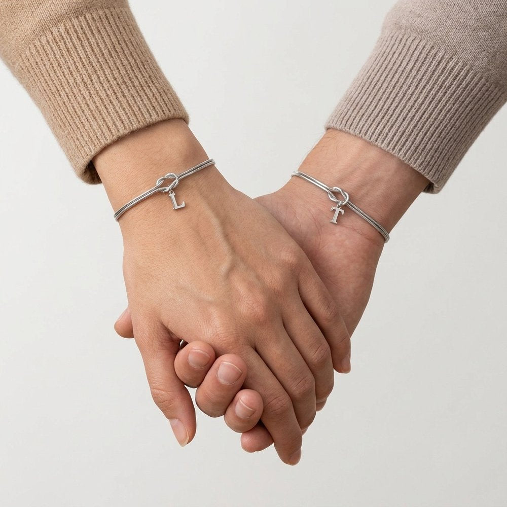 Duo de bracelet noeud porté par un couple qui se tient la main, une initiale suspendue à chaque nœud